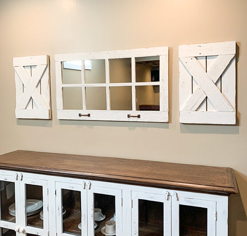 May include: Three white farmhouse style mirrors with a woodgrain finish. The centre mirror is a large rectangular window pane style mirror with nine square panes. The two smaller mirrors are square and have a criss-cross design.