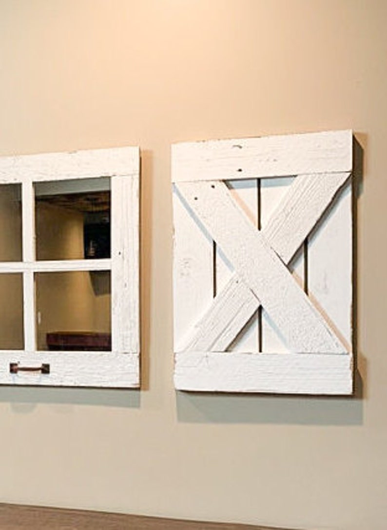 May include: Two white painted wooden wall decor pieces. One is a window frame with a pane of glass and the other is a barn door style with an X design.