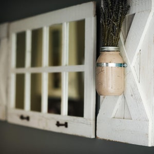 May include: Two white painted wooden window frames with glass panes, one with a mason jar filled with dried lavender and a metal band, mounted on a gray wall.