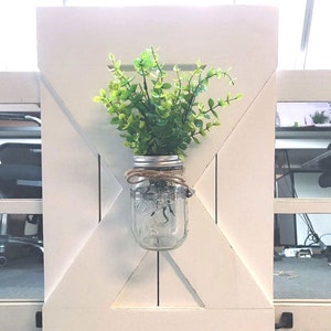 May include: White wooden farmhouse style wall decor with a mason jar filled with green faux greenery hanging in the centre.
