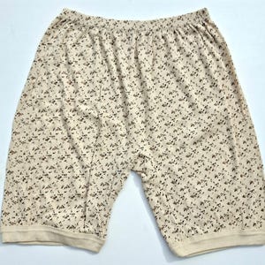 Peut inclure: Shorts crème avec un motif répété de petites fleurs brunes. Le short a une taille élastique et est fait d'un tissu côtelé. Les ouvertures de jambes sont finies avec une bande crème unie.