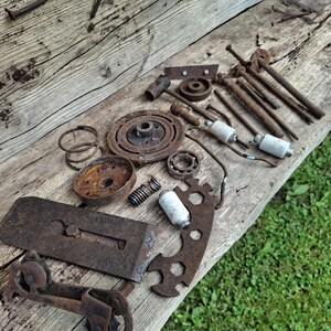 Könnte beinhalten: Eine Sammlung rostiger Metallmaschinenteile, darunter Zahnräder, Federn und Bolzen, die auf einer verwitterten Holzoberfläche angeordnet sind. Die Komponenten variieren in Größe und Form und weisen unterschiedliche Korrosionsgrade auf.