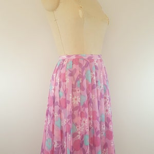 May include: A pink pleated skirt with a floral print featuring pink, purple, and blue flowers. The skirt is on a dress form.