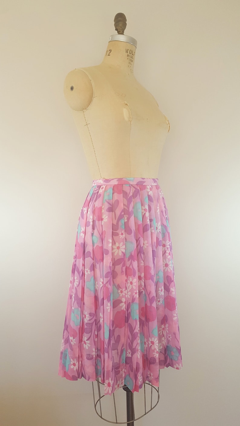 May include: A pink pleated skirt with a floral print featuring pink, purple, and blue flowers. The skirt is on a dress form.