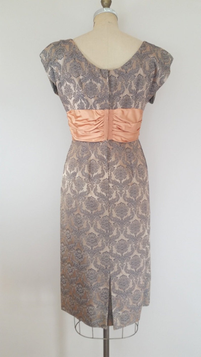 May include: A vintage dress with a gray and peach brocade pattern. The dress has a fitted bodice and a full skirt. It features a peach satin sash around the waist.