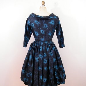 May include: A black and blue vintage dress with a floral print. The dress has a bateau neckline, 3/4 sleeves, and a full skirt.