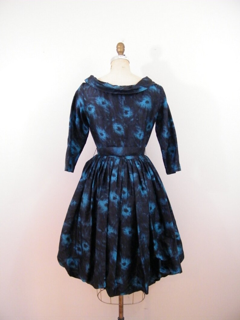 May include: A black and blue vintage dress with a floral print. The dress has a bateau neckline, 3/4 sleeves, and a full skirt.