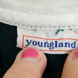 Puede incluir: Primer plano de una camisa verde oscuro con cuello blanco y una etiqueta blanca que dice "youngland" en letras azules.