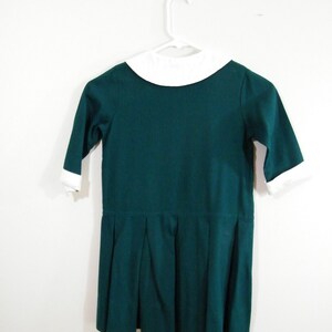 Puede incluir: Un vestido verde oscuro con un cuello blanco Peter Pan y una falda plisada.