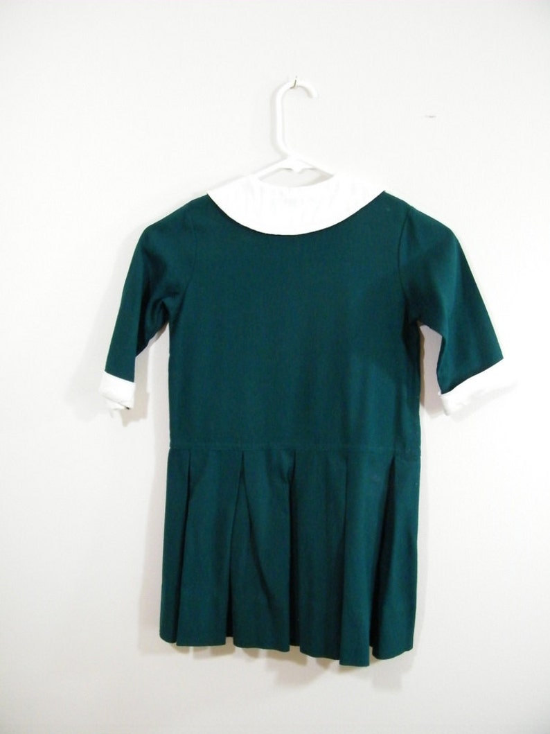 Puede incluir: Un vestido verde oscuro con un cuello blanco Peter Pan y una falda plisada.