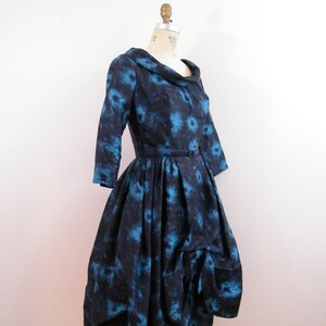 May include: A blue and black vintage dress with a floral print and a cinched waist. The dress has a full skirt and a scoop neckline.