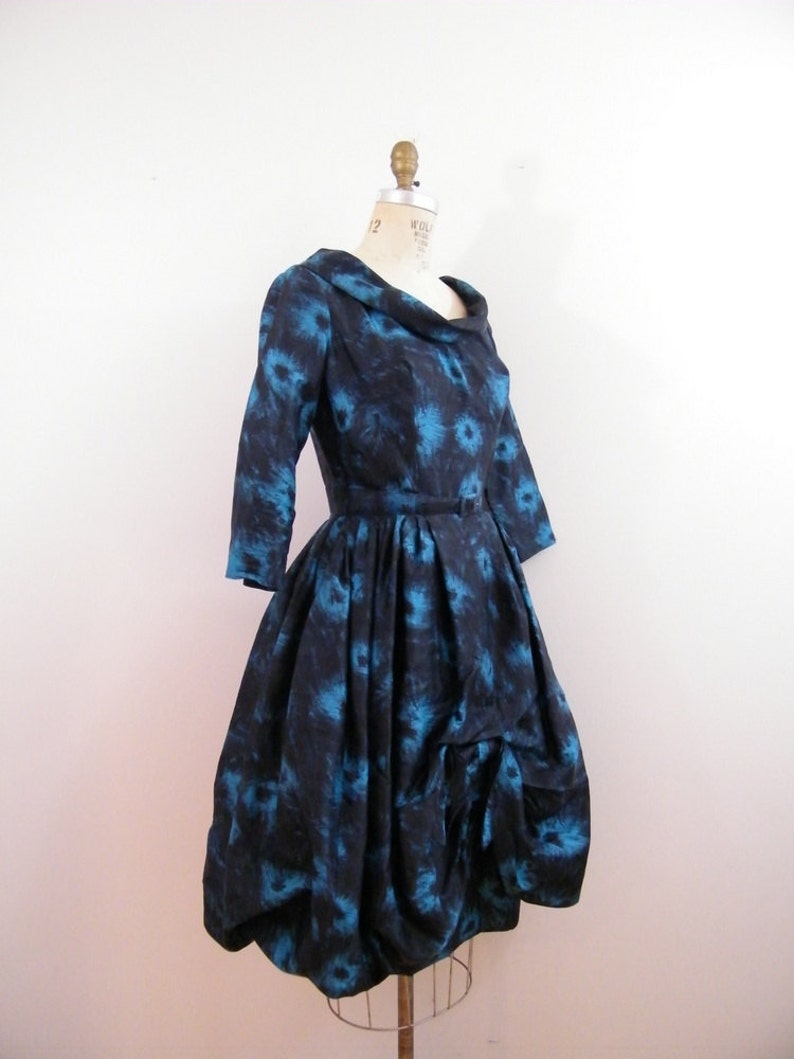 May include: A blue and black vintage dress with a floral print and a cinched waist. The dress has a full skirt and a scoop neckline.
