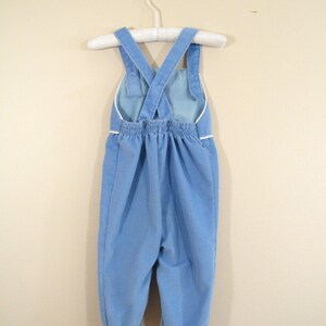 Op de afbeelding: Blauwe corduroy broek met witte bies en verstelbare schouderbanden. De broek hangt aan een witte hanger.