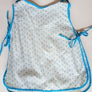 May include: A white baby bib with a blue floral pattern and a blue trim. The bib has ties on the sides.