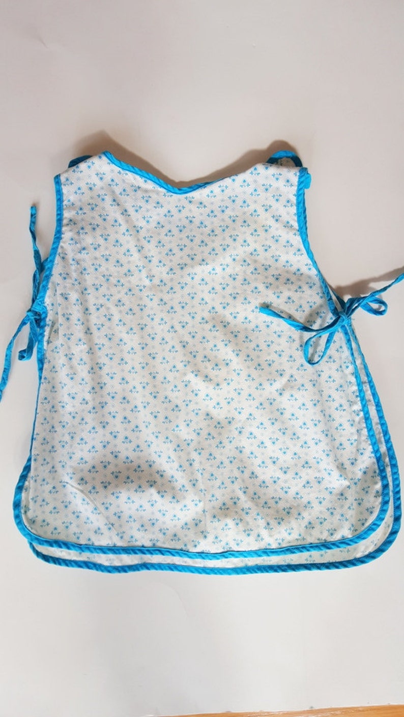 May include: A white baby bib with a blue floral pattern and a blue trim. The bib has ties on the sides.