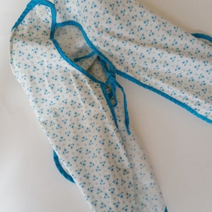 May include: A white fabric baby bib with a blue trim and a small white button. The bib has a blue and white floral pattern.