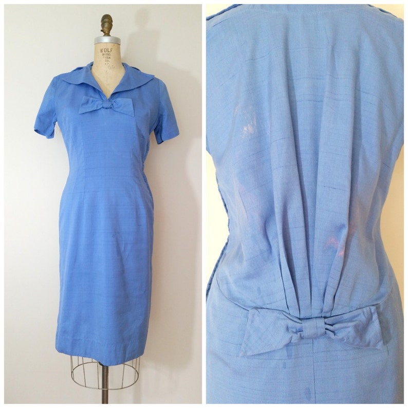 K&ouml;nnte beinhalten: Ein hellblaues Kleid mit einer Schleife am Ausschnitt und einer Schleife am R&uuml;cken. Das Kleid hat kurze &Auml;rmel und eine figurbetonte Silhouette.