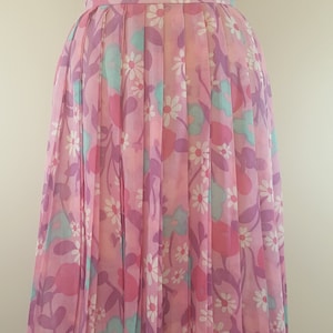 May include: A pink pleated skirt with a floral print featuring white daisies, pink and purple flowers, and teal leaves.