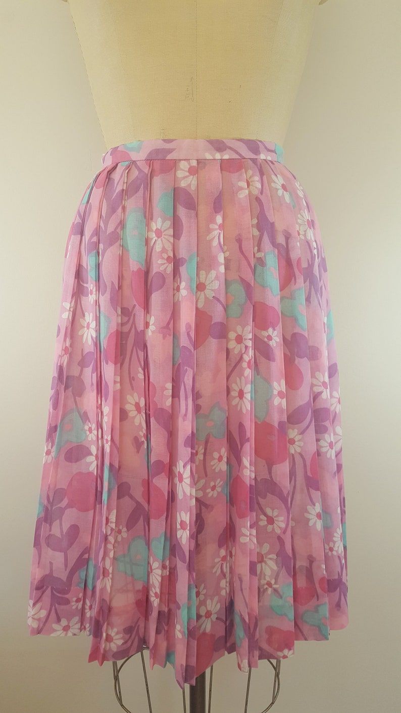 May include: A pink pleated skirt with a floral print featuring white daisies, pink and purple flowers, and teal leaves.