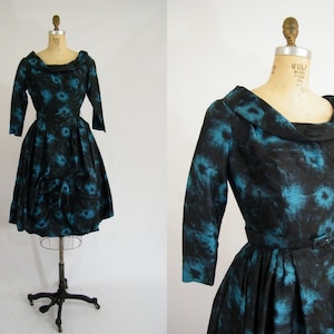 May include: A black and teal vintage dress with a cowl neck and a belt. The dress has a floral pattern and a full skirt.