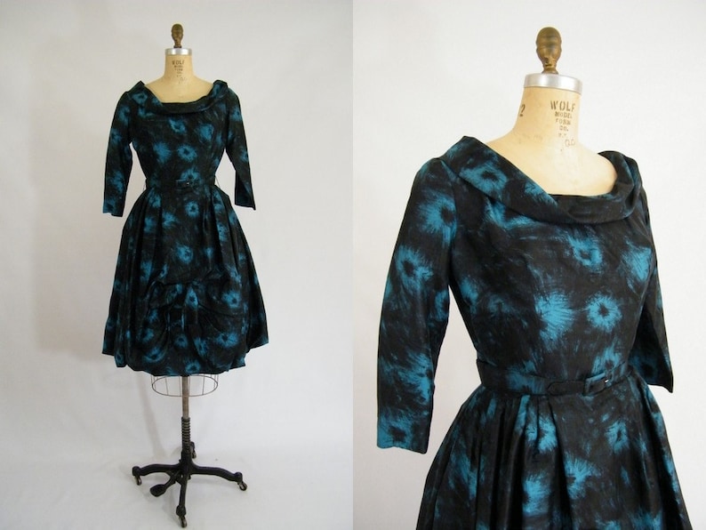 May include: A black and teal vintage dress with a cowl neck and a belt. The dress has a floral pattern and a full skirt.