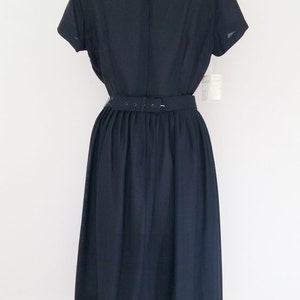 May include: A navy blue dress with a fitted bodice and a full skirt. The dress has a belt at the waist and short sleeves.