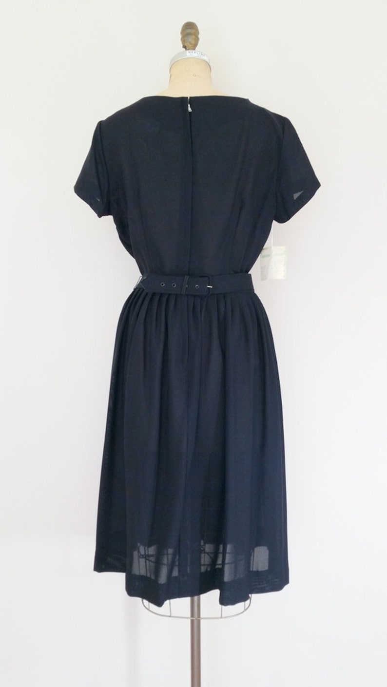 May include: A navy blue dress with a fitted bodice and a full skirt. The dress has a belt at the waist and short sleeves.