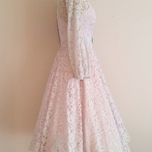 May include: A pink lace dress with long sleeves and a fitted bodice. The dress has a full skirt and a delicate floral pattern.