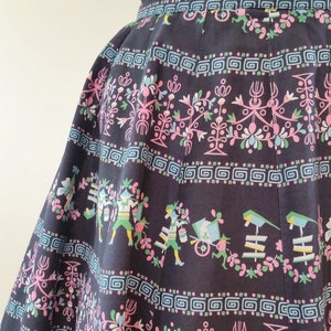 K&ouml;nnte beinhalten: Ein schwarzer Rock mit einem bunten floralen und geometrischen Muster. Das Muster zeigt rosa, blaue und gr&uuml;ne Blumen und geometrische Formen.