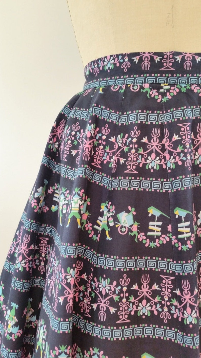 K&ouml;nnte beinhalten: Ein schwarzer Rock mit einem bunten floralen und geometrischen Muster. Das Muster zeigt rosa, blaue und gr&uuml;ne Blumen und geometrische Formen.