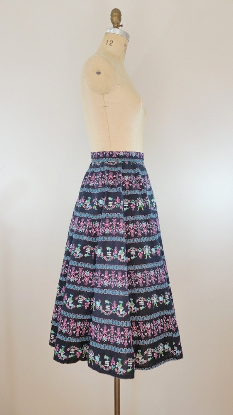 K&ouml;nnte beinhalten: Ein schwarzer Midirock mit einem bunten floralen und geometrischen Muster. Der Rock ist weit und hat eine hohe Taille.