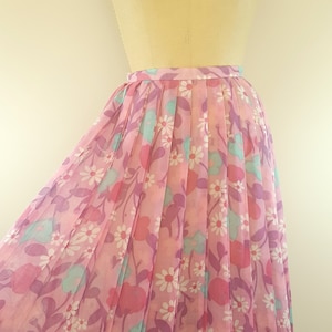 May include: A pink pleated skirt with a floral print featuring white daisies, pink and purple flowers, and blue leaves.