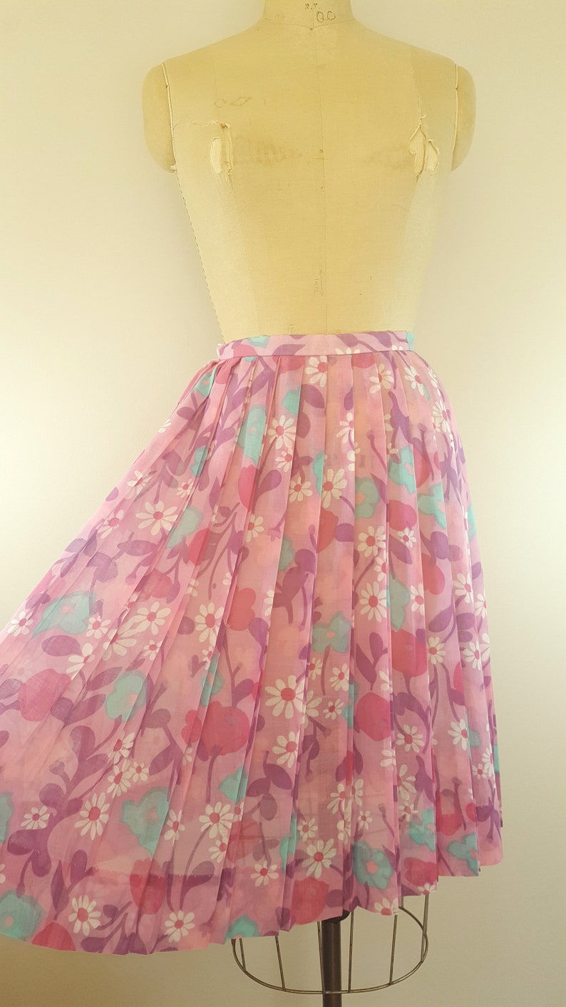 May include: A pink pleated skirt with a floral print featuring white daisies, pink and purple flowers, and blue leaves.