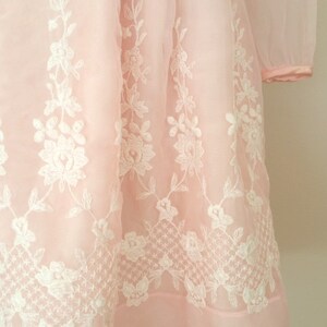 May include: A pink dress with white floral embroidery. The dress has long sleeves and a full skirt.
