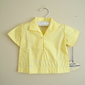 May include: A yellow short-sleeved button-down shirt with a white swan embroidered on the front. The shirt has a scalloped hem and a tag that reads "Annette&reg;  Permanently Pressed".