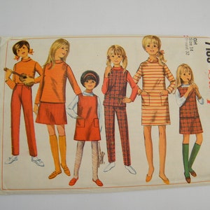 Könnte beinhalten: Simplicity Schnittmuster Nummer 7189 für Mädchen in den Größen 14 und 12. Das Schnittmuster enthält fünf verschiedene Outfits, darunter einen karierten Latzrock, ein gestreiftes Kleid und einen roten Rock mit passendem Pullover.