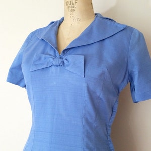 K&ouml;nnte beinhalten: Ein hellblaues Kleid mit Schleife am Ausschnitt und kurzen &Auml;rmeln. Das Kleid befindet sich auf einer Kleiderpuppe.