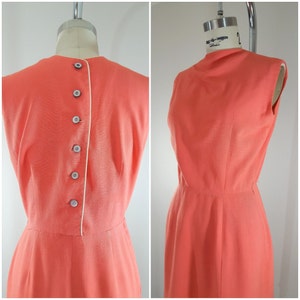 Puede incluir: Un vestido coral sin mangas con un ribete blanco en la espalda y una fila de botones. El vestido tiene un corpi&ntilde;o ajustado y una falda ligeramente acampanada.