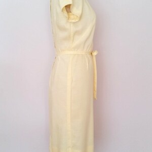 May include: A pale yellow sleeveless dress with a sash tie at the waist. The dress is on a dress form.