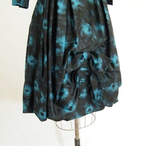 May include: A black and teal vintage dress with a gathered skirt and a bow detail. The dress has a floral print.