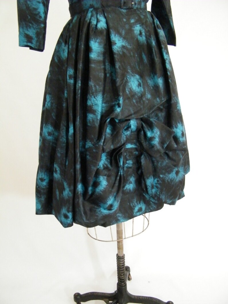 May include: A black and teal vintage dress with a gathered skirt and a bow detail. The dress has a floral print.