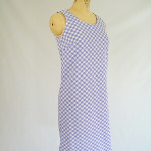 May include: A sleeveless dress with a white and lavender gingham pattern. The dress is fitted and has a straight skirt.