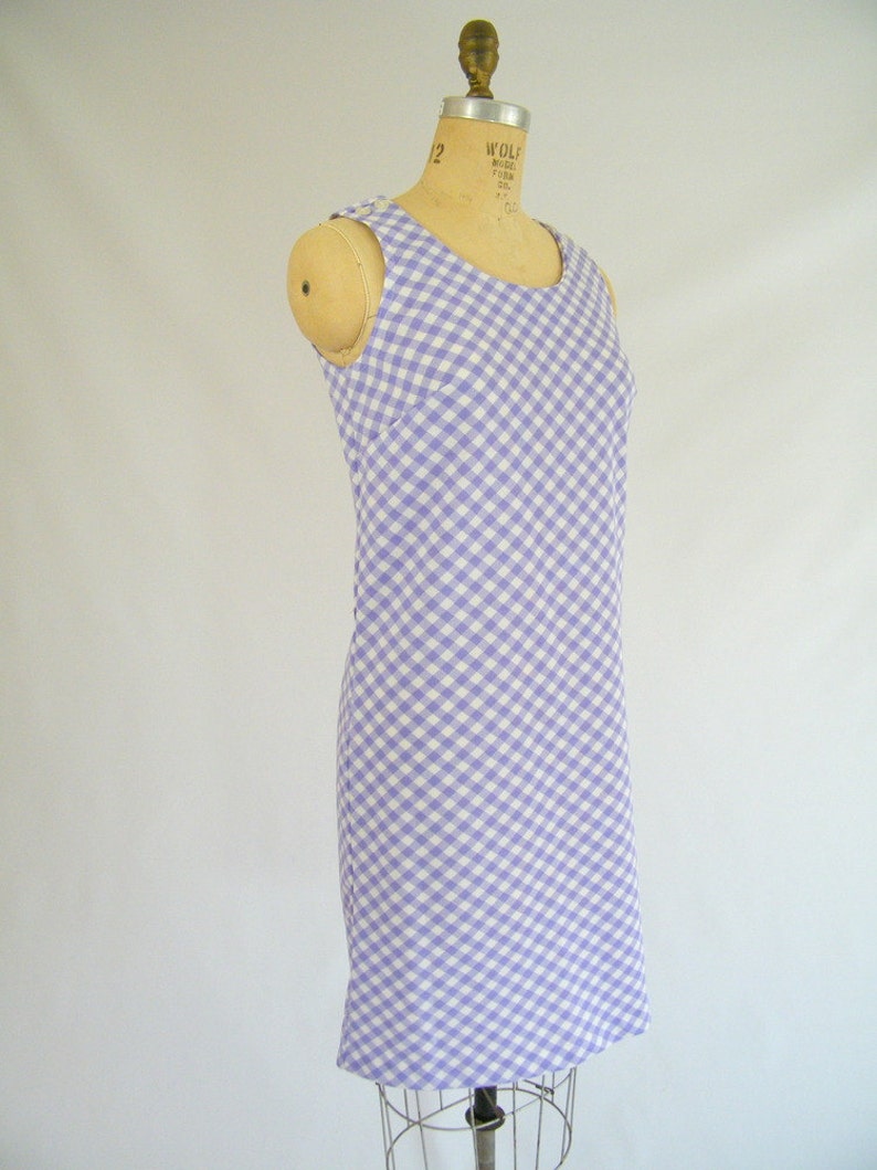 May include: A sleeveless dress with a white and lavender gingham pattern. The dress is fitted and has a straight skirt.