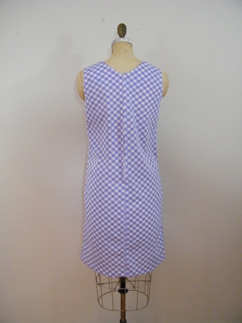 May include: A sleeveless dress with a white and purple gingham pattern. The dress is fitted and has a straight skirt.