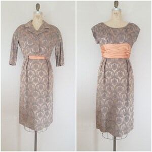 May include: A vintage two-piece dress set in a brown and silver damask pattern. The dress has a scoop neck and a matching jacket with a collar and three-quarter sleeves. Both pieces feature a peach-colored satin sash.