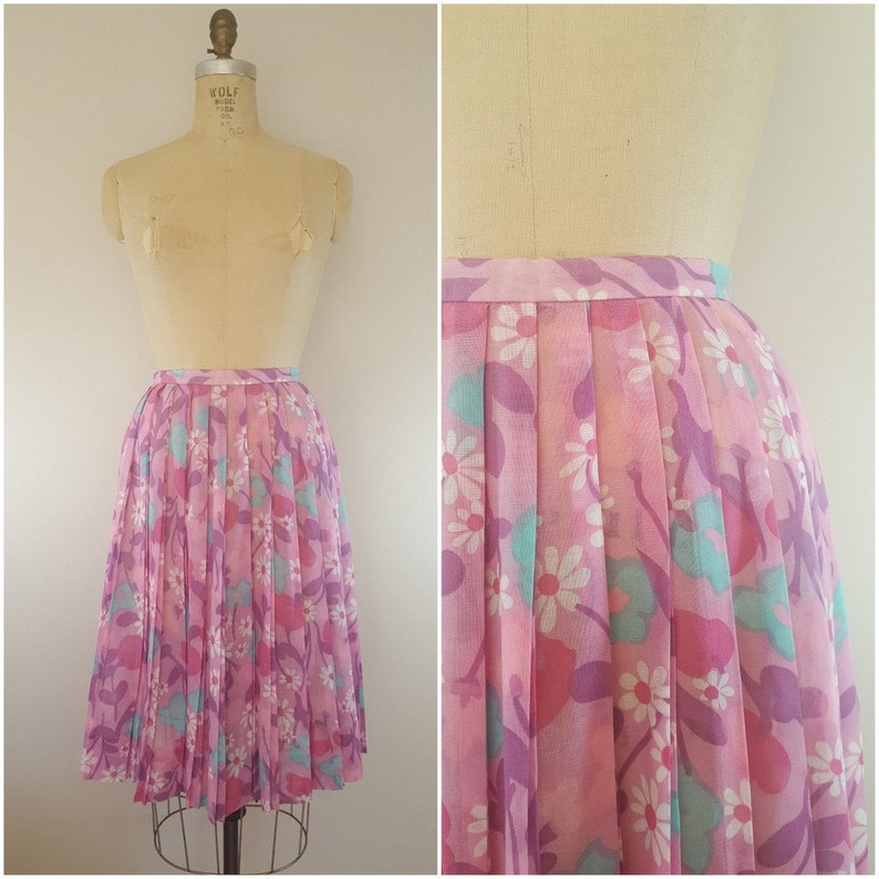 May include: A pink pleated skirt with a floral print featuring white daisies, purple leaves, and light blue accents.