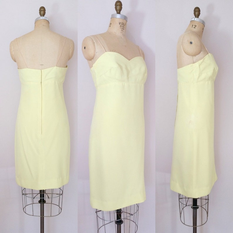 Puede incluir: Un vestido sin mangas de color amarillo p&aacute;lido con un escote de coraz&oacute;n. El vestido es entallado y tiene una falda recta. Se muestra sobre un fondo blanco.