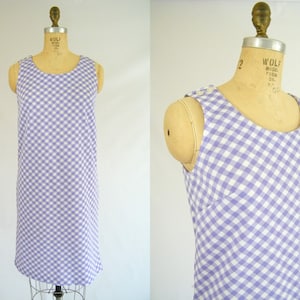May include: A sleeveless dress with a white and purple gingham pattern. The dress has a scoop neck and a straight silhouette.