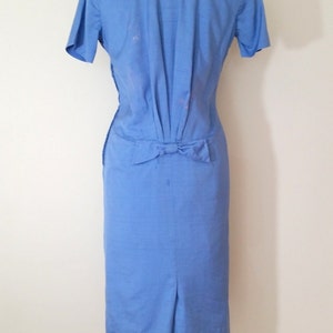 K&ouml;nnte beinhalten: Ein hellblaues Kleid mit einer Schleife in der Taille. Das Kleid hat kurze &Auml;rmel und eine figurbetonte Silhouette.