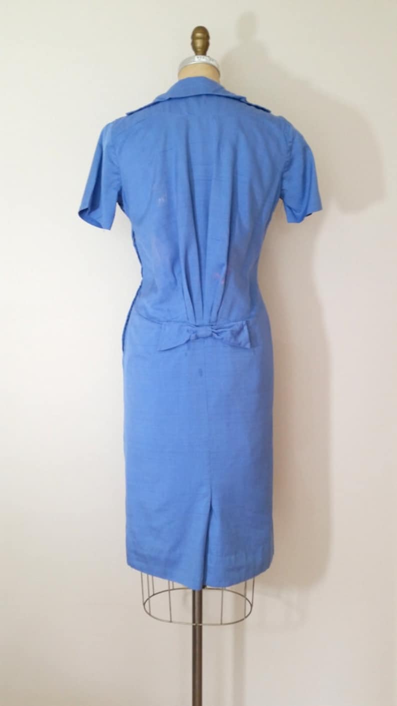 K&ouml;nnte beinhalten: Ein hellblaues Kleid mit einer Schleife in der Taille. Das Kleid hat kurze &Auml;rmel und eine figurbetonte Silhouette.